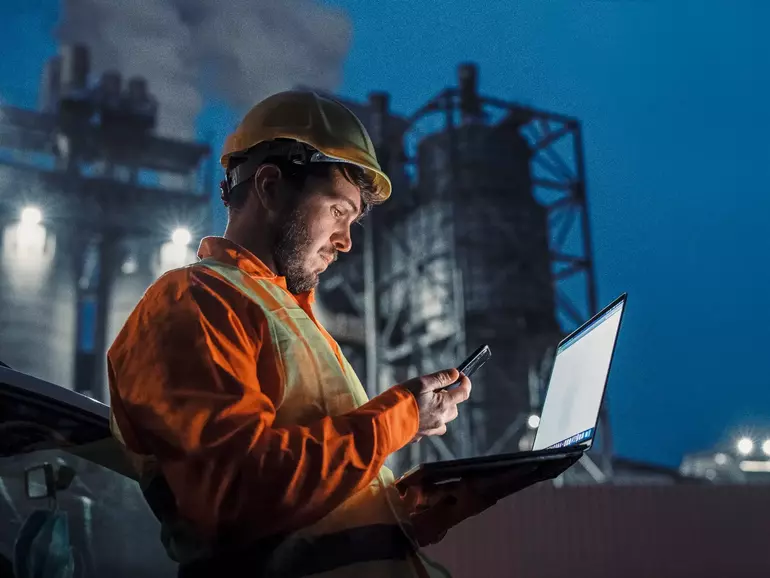 Engineer working nightshift and using technology in front of petroleum industrial factory Engineer working nightshift and using technology in front of petroleum industrial factory
