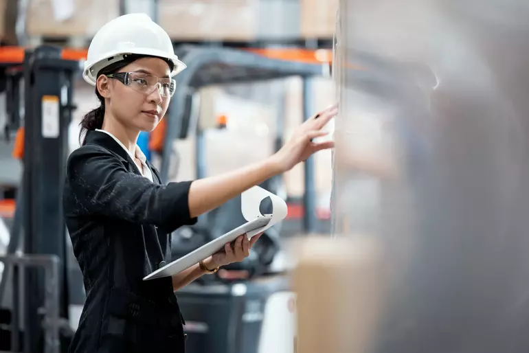 A young female in a polo shirt uniform checking the product in a shelf rack asian staff taking inventory in a distribution warehouse and supply chain management solution A young female in a polo shirt uniform checking the product in a shelf rack asian staff taking inventory in a distribution warehouse and supply chain management solution