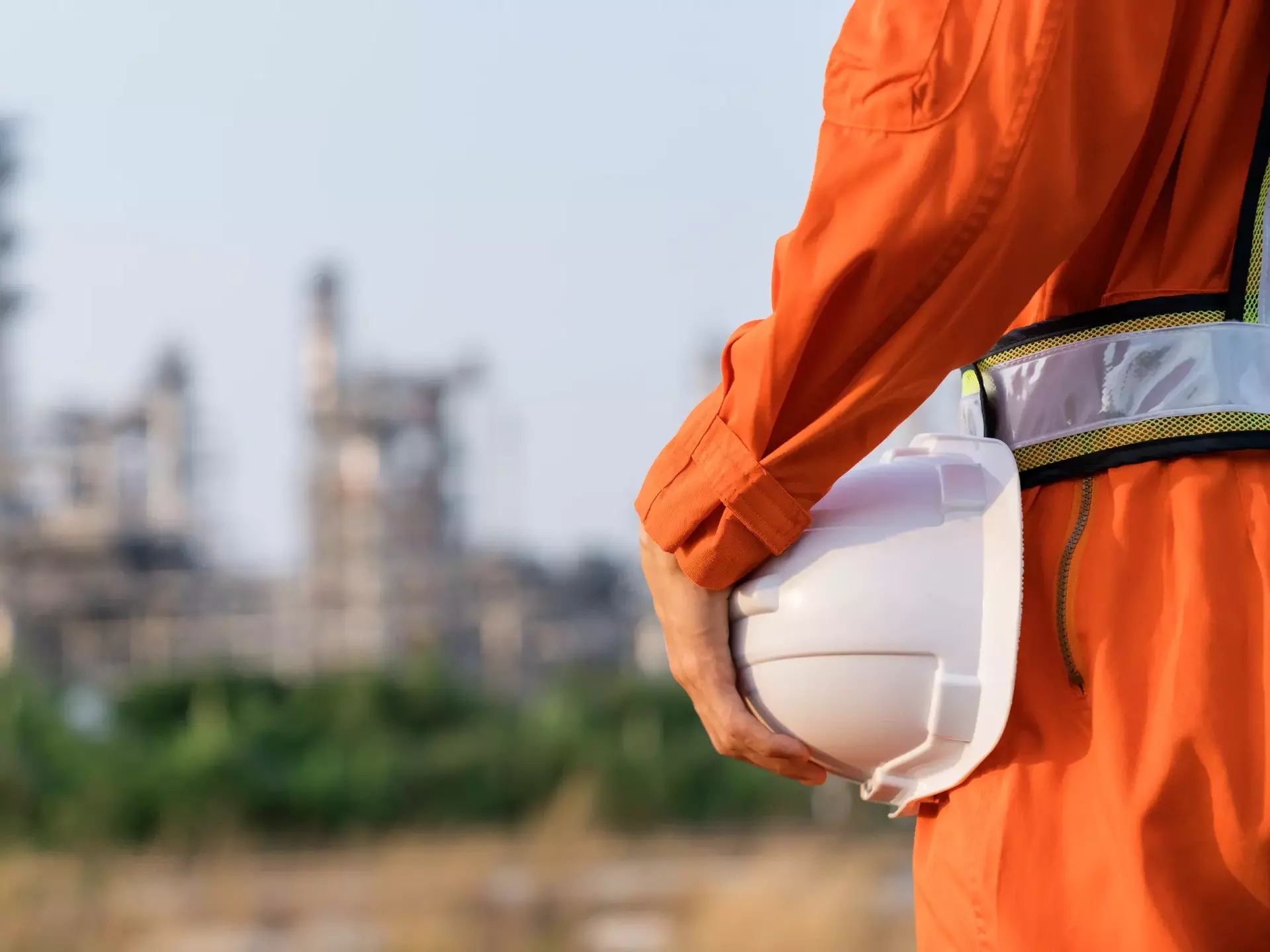 Rear view of engineer man in suite stand holding white safety helmet and blur refinery oil background Rear view of engineer man in suite stand holding white safety helmet and blur refinery oil background