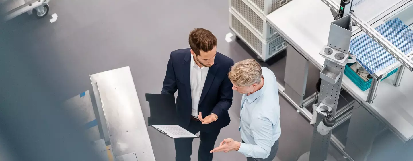 Two businessmen with clipboard talking in a factory