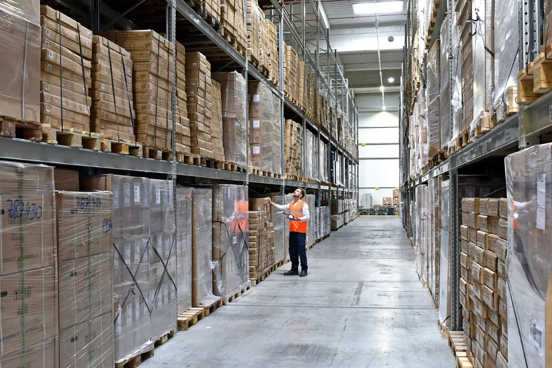 Man in factory hall wearing safety vest using barcode scanner